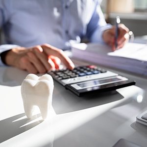 a man calculating cost and a small tooth on a desk