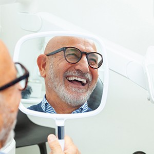 a man in a dental office looking in a handheld mirror and smiling