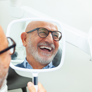 Man smiling in the mirror with new dental 