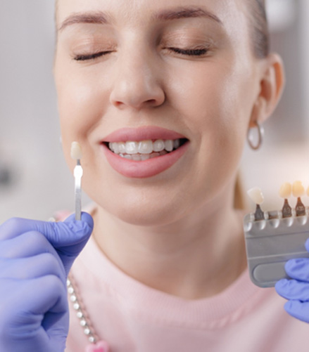 Tweezers holding a veneer against a background of lying veneers