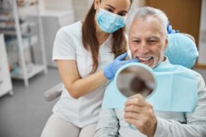 Senior man admiring teeth in dentist's chair.
