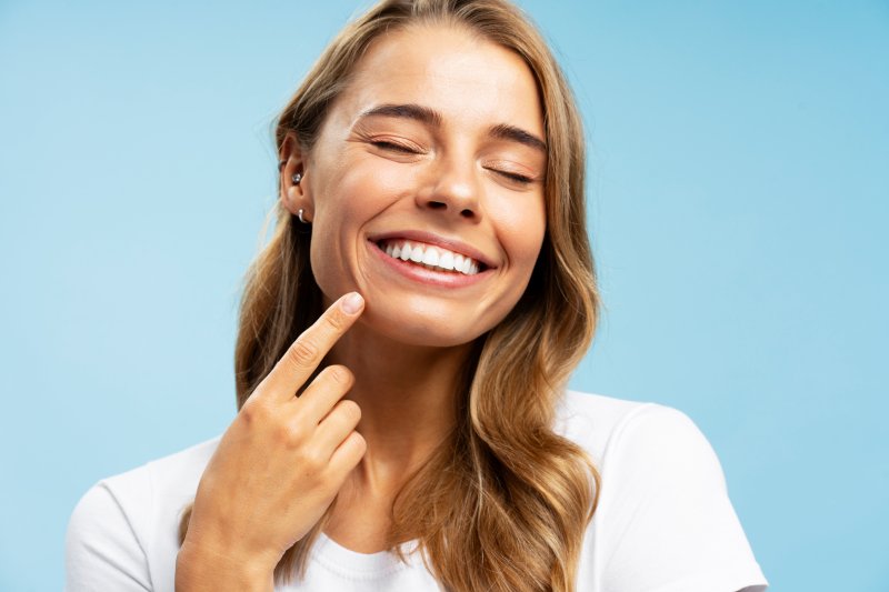 A smiling woman closing her eyes and pointing to her whiter teeth